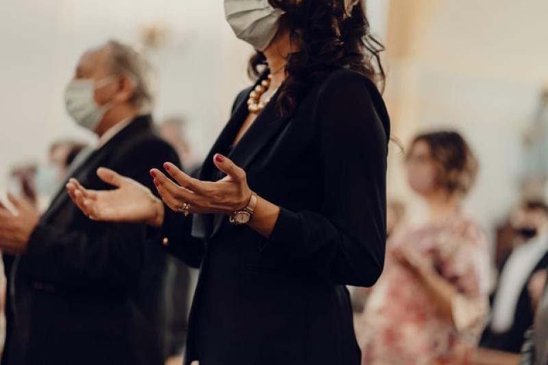 Woman in church wearing a face mask and praying with her hands outstretched